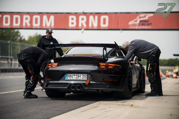 Drei Boxencrew-Mitglieder beugen sich über einen dunklen Porsche vor dem Schriftzug Automotodrom Brno