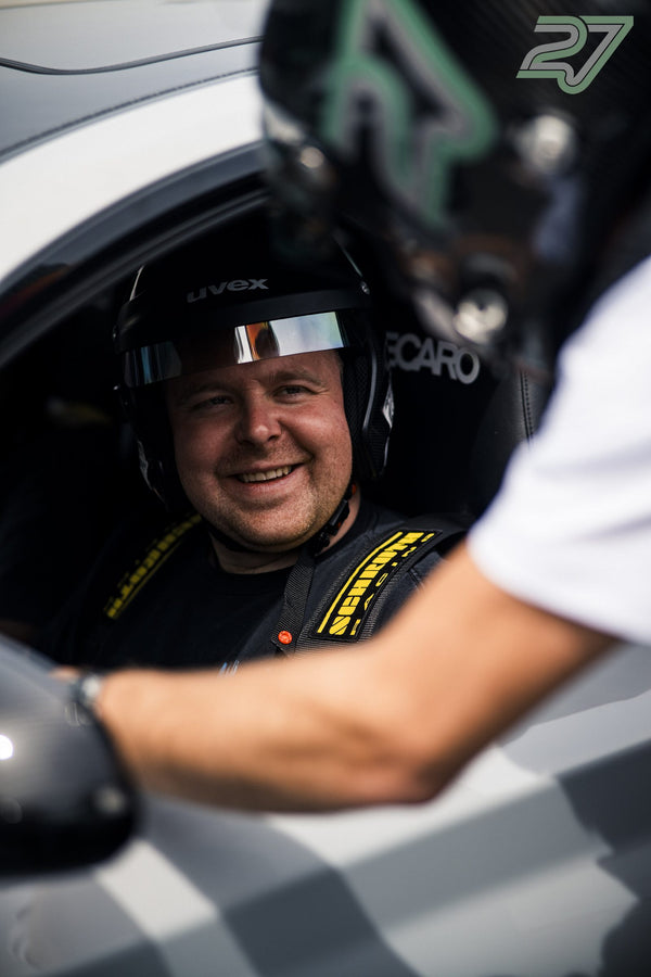 Ein lächelnder Fahrer im Helm blickt im Cockpit zu einer Person, die ihm die Hand reicht