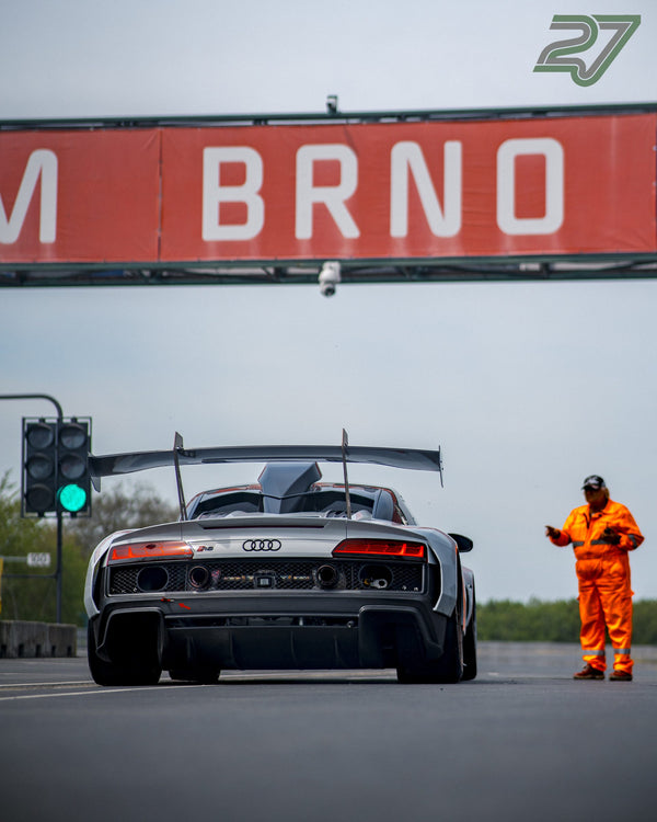 Weißer Audi R8 GT3 rollt unter dem BRNO-Schriftzug, während ein Streckenposten in Orange Zeichen gibt