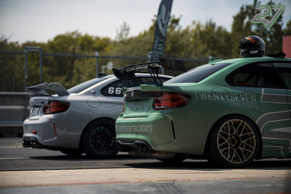Ein silberner und ein mintgrüner BMW M2 mit Twentyseven-Trackdays-Schriftzug stehen Heck an Heck