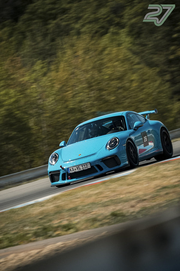 Hellblauer Porsche 911 GT3 mit Startnummer 26 fährt frontal durch eine Waldkurve in Brünn