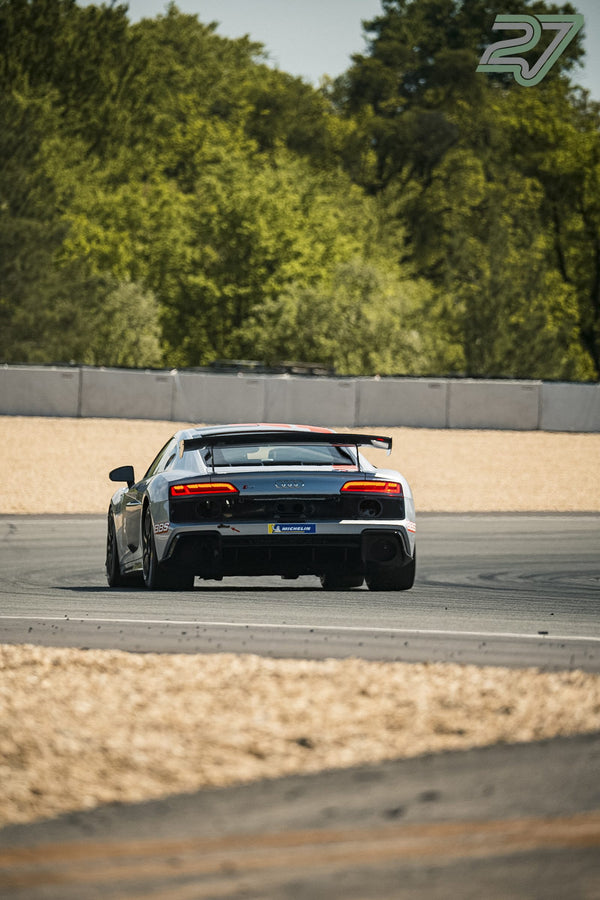 Silberner Audi R8 GT3 bremst mit aufleuchtenden Rückleuchten von hinten vor einer Kurve