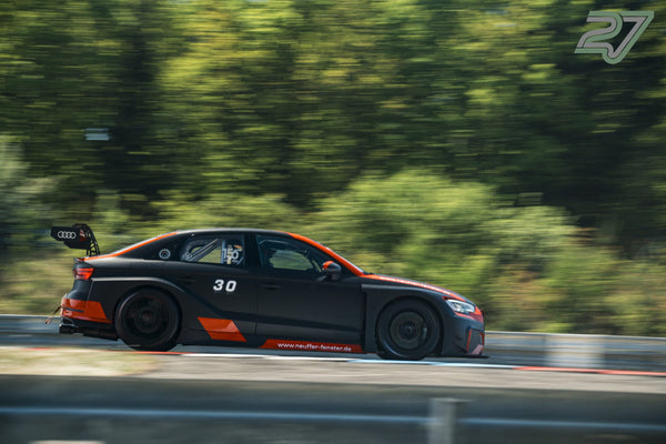 Schwarz-oranger Audi RS3 TCR rast in scharfer Seitenfahrt an verschwommenen Bäumen vorbei