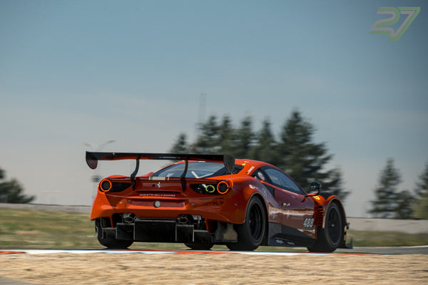 Orangeroter Ferrari 488 GT3 verlässt hecknah eine Kurve, dahinter einzelne Kiefern vor blauem Himmel