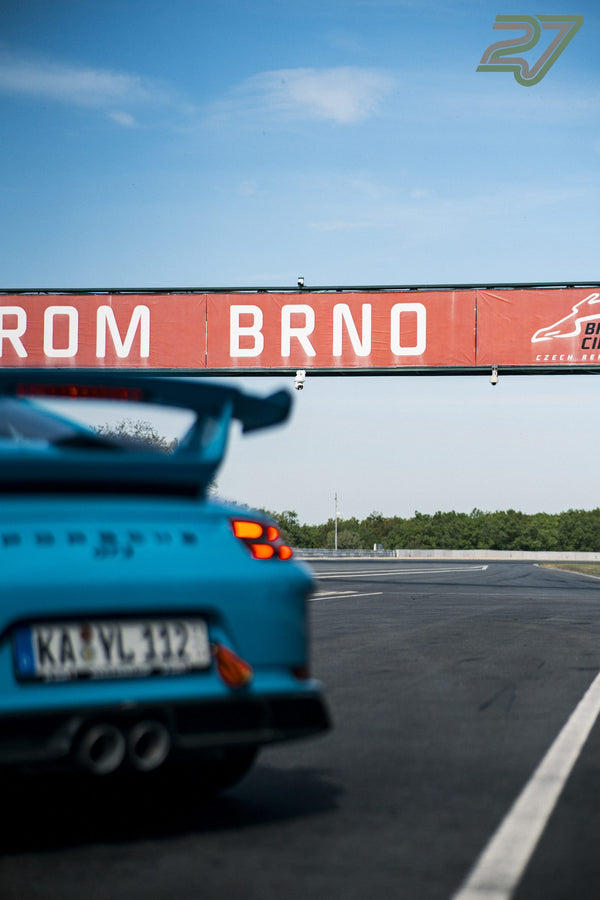 Türkiser Porsche 911 fährt unter dem Streckentorbogen mit Brünn-Schriftzug hindurch