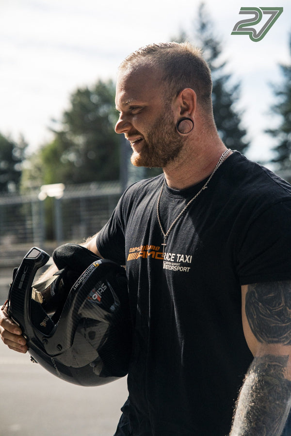 Bärtiger, tätowierter Mann mit Ohr-Plug lächelt und hält einen schwarzen Helm unter dem Arm
