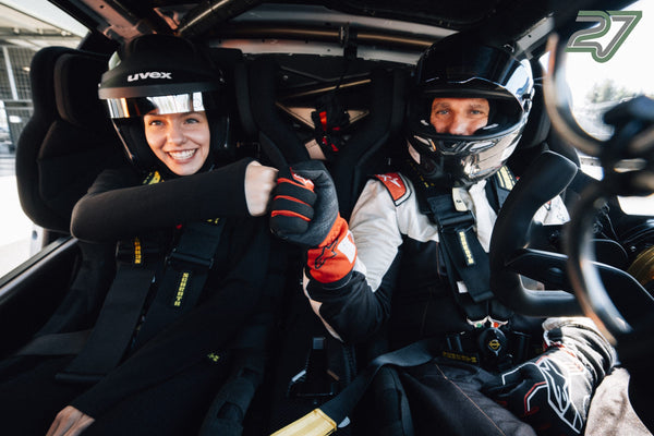 Junge Frau und Fahrer im Helm stoßen lachend die Fäuste im Cockpit des Rennwagens zusammen