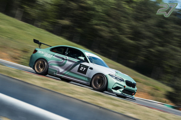 Mintgrüner BMW M2 im knackscharfen Seitenprofil rollt einen Streckenabschnitt am Waldhang hinab