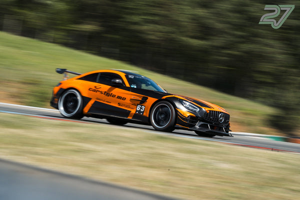 Orange-schwarzer Mercedes-AMG GT zieht scharf im Seitenprofil den Hang hinunter, Wald verschwimmt