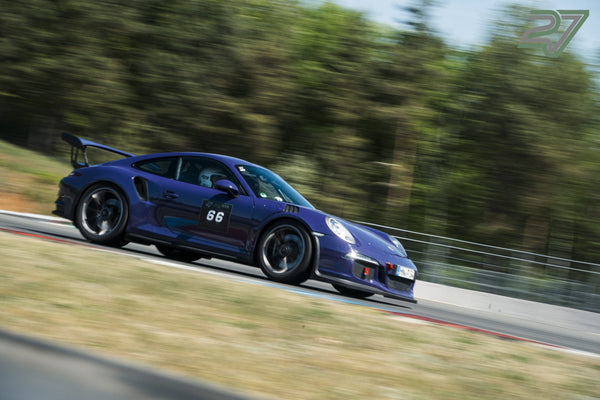 Dunkelblauer Porsche 911 GT3 zieht scharf im Seitenprofil am dichten Nadelwald vorbei