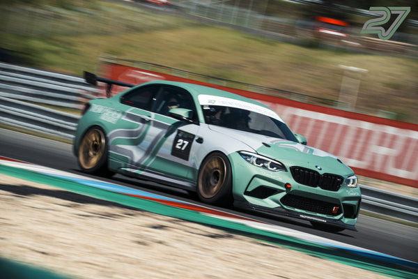 Mintgrüner BMW M2 kommt frontal aus einer Kurve, im Hintergrund verschwimmt eine rote Bande