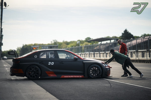 Zwei Männer schieben einen schwarz-roten Audi RS3 LMS durch die sonnige Boxengasse