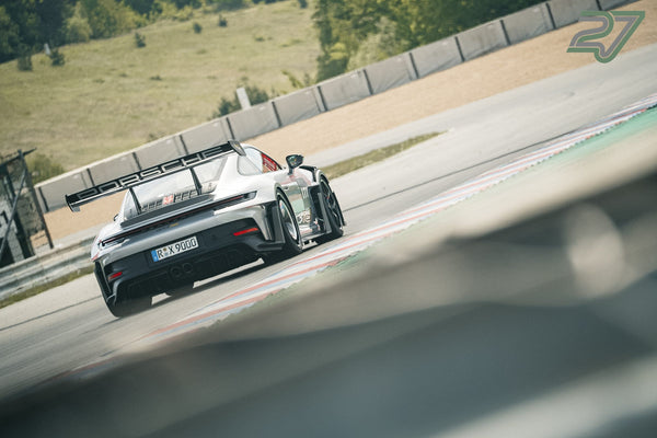 Weißer Porsche 911 mit großem Heckflügel kurvt heckseitig aus einer Kurve heraus