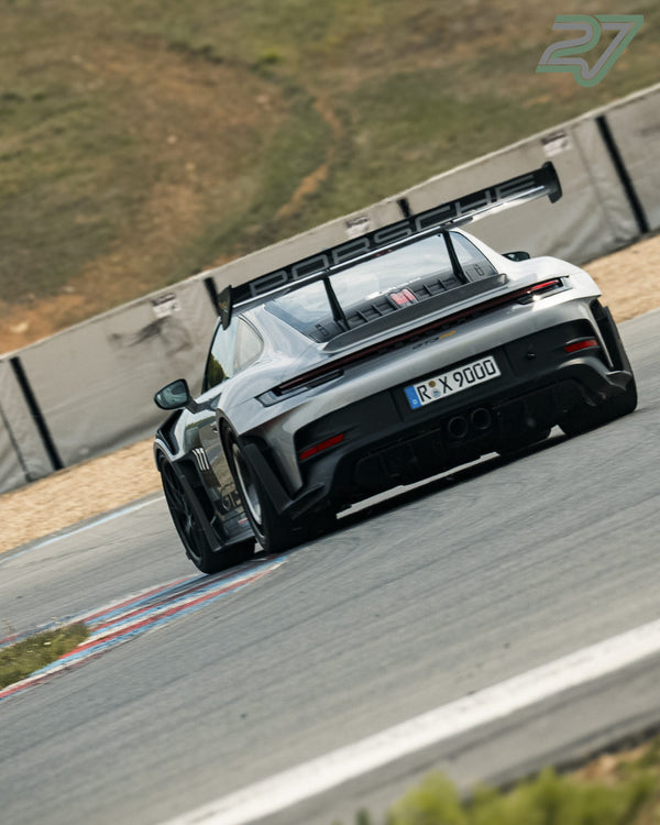 Silberner Porsche 911 mit Heckflügel und Porsche-Schriftzug fährt eng um eine Kurve