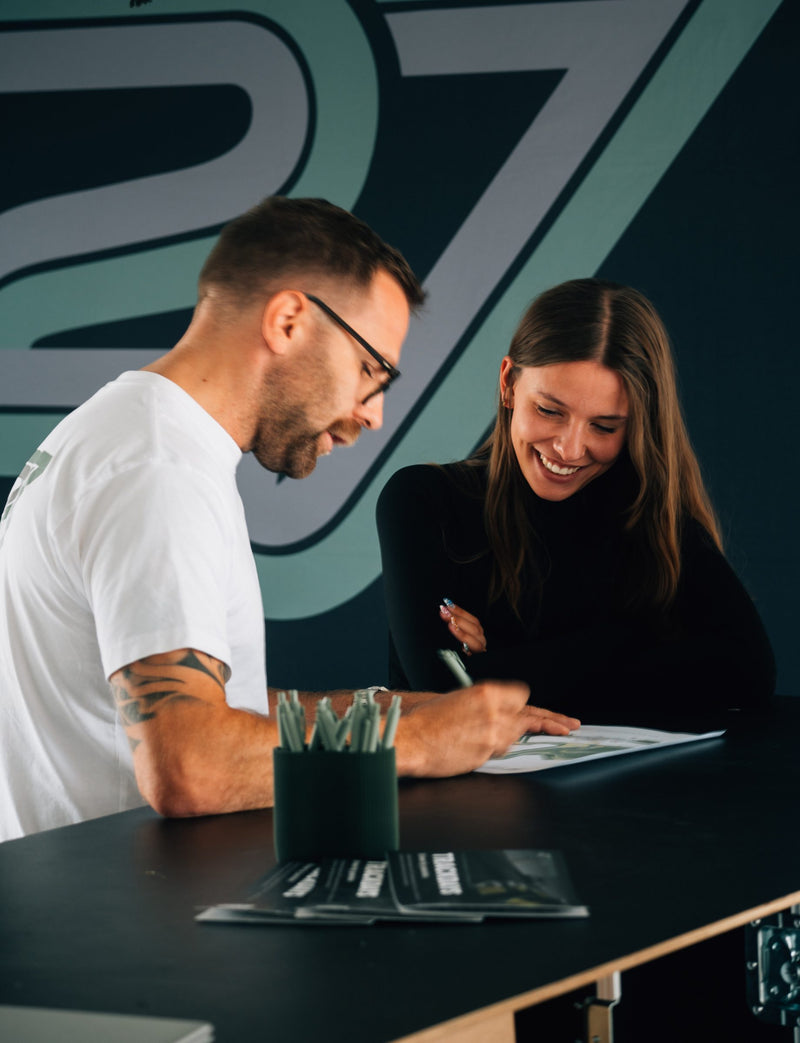 Coach going through a document at the counter with a smiling participant in front of the TWENTYSEVEN wall