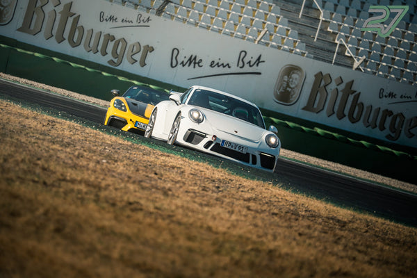 Weißer Porsche 911 GT3 fährt dicht vor einem gelb-schwarzen Sportwagen an der Werbebande vorbei
