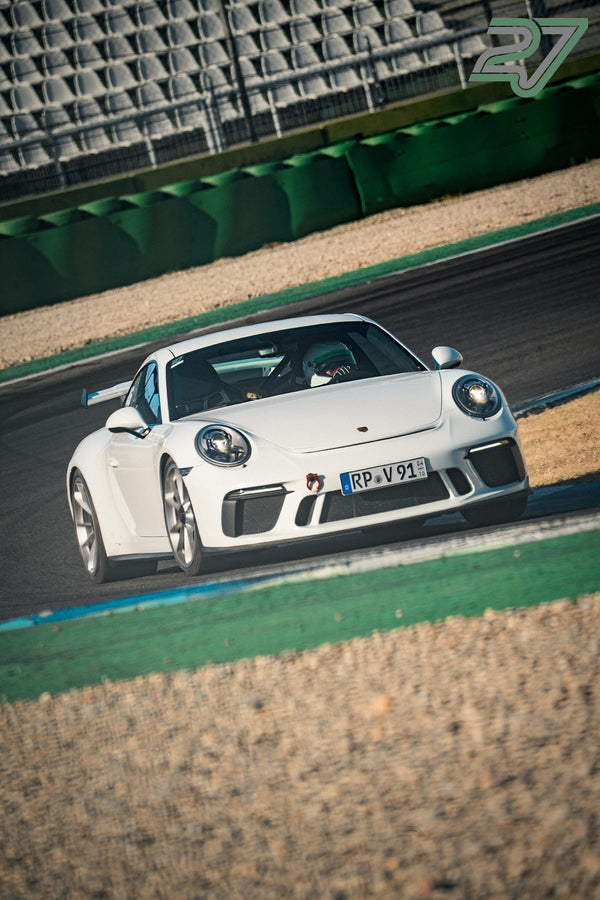 Reinweißer Porsche 911 GT3 bremst frontal in die Kurve, der Fahrer trägt einen hellen Helm
