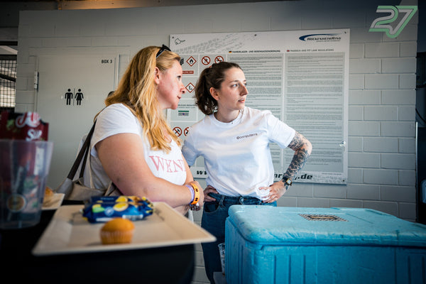 Zwei Teilnehmerinnen mit Snacks und Kühlbox stehen vor der Boxenordnung des Hockenheimrings