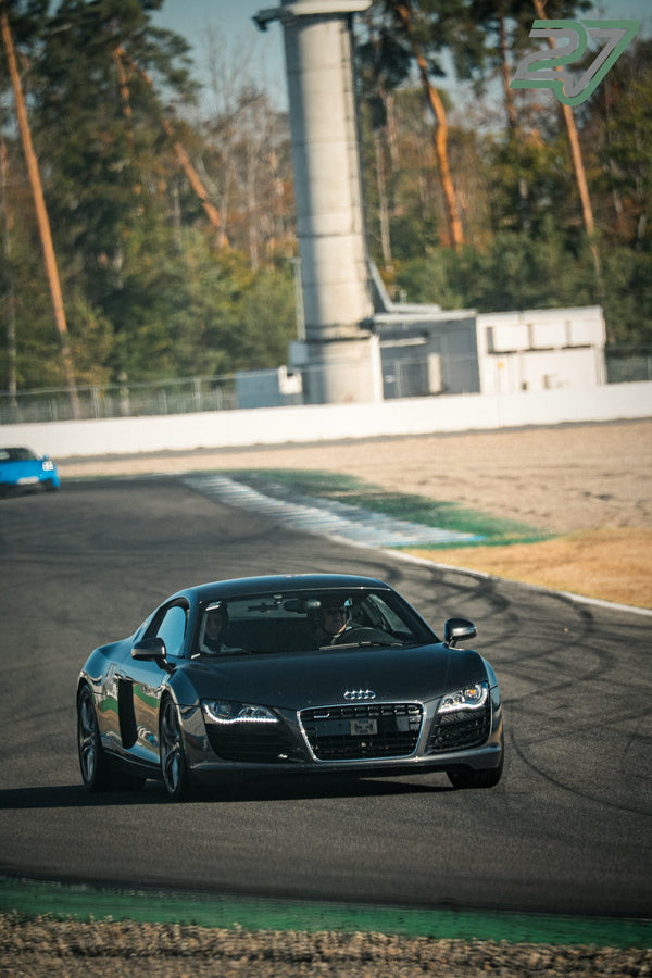 Dunkler Audi R8 nähert sich schräg von vorne der Kamera, im Hintergrund ein Turm verschwimmt