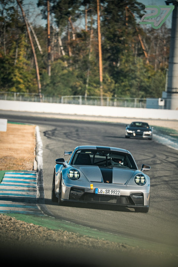 Silberner Porsche 911 GT3 mit schwarzem Streifen auf Haube und Dach fährt in die Kurve