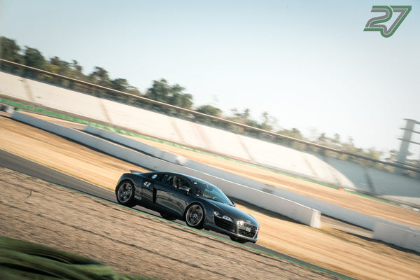 Dunkelgrauer Audi R8 gleitet im Seitenprofil an der verschwommenen Tribüne vorbei, helles Tageslicht