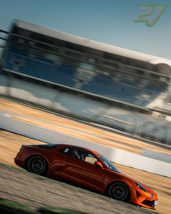 Orangeroter Alpine A110 gleitet im Seitenprofil an der verschwommenen Tribüne vorbei