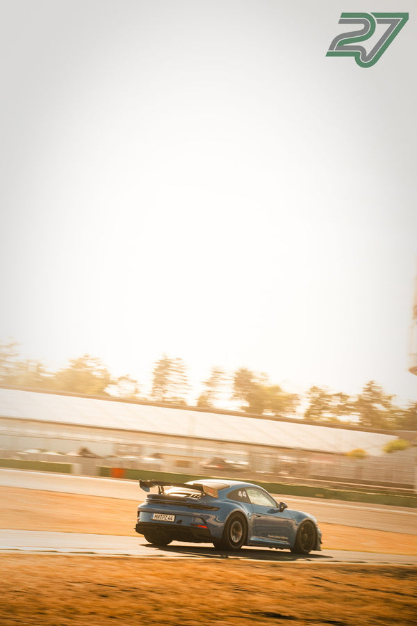 Graublauer Porsche 911 GT3 RS fährt im Gegenlicht der Abendsonne durch eine Kurve, Staub über der Strecke