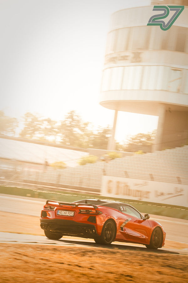 Orangerotes Corvette-Coupé rollt vor dem beleuchteten Kontrollturm des Hockenheimrings im Abendlicht