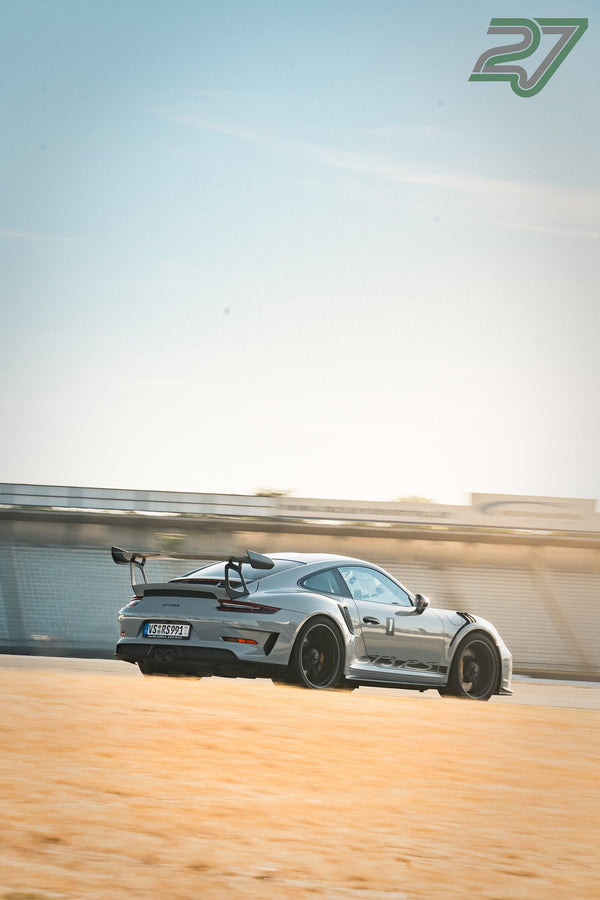 Silberner Porsche 911 GT3 RS mit großem Heckflügel rollt durch eine Kurve, blauer Himmel im Hintergrund