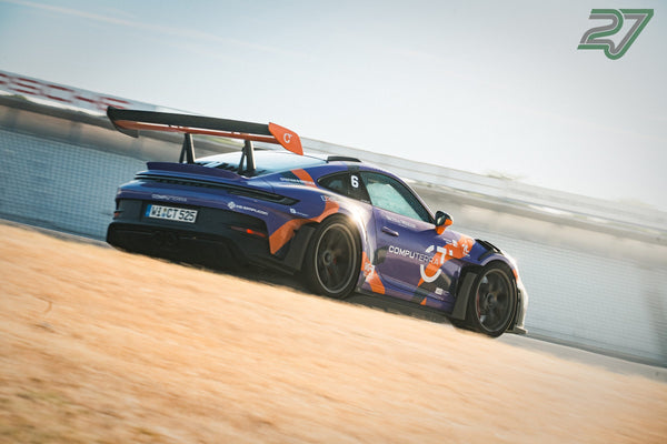 Lila-oranger Porsche GT3 Cup-Renner mit auffälliger Sponsoren-Livree kurvt durch den Staub am Streckenrand