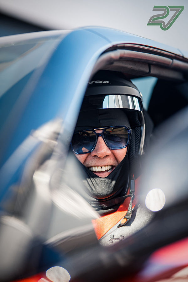 Eine Person mit Sonnenbrille im Helm lacht breit im Cockpit, Gurtzeug leuchtet orange