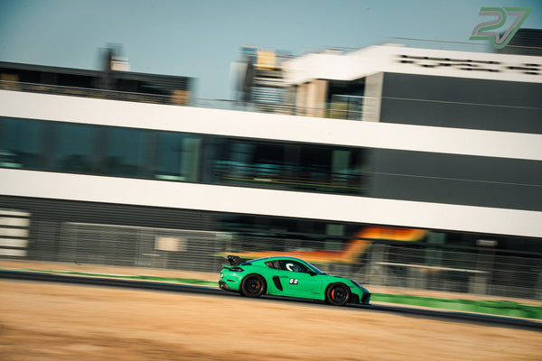 Grüner Porsche mit GT4RS-Aufkleber gleitet im Schwenk an der modernen Fahrerlager-Fassade vorbei