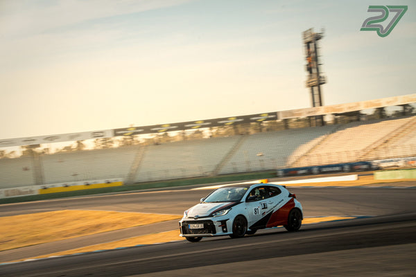 Weißer Toyota GR Yaris mit roter Rennlackierung fährt schräg von vorne durch eine schnelle Kurve