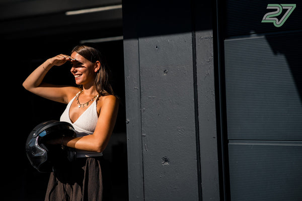 Eine Frau mit Helm unterm Arm hält die Hand vors Gesicht und lächelt in die Sonne