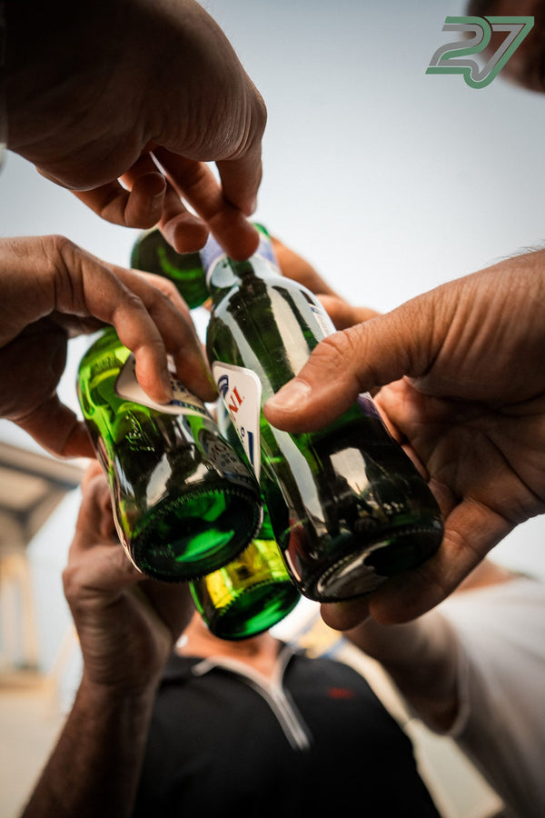 Nahaufnahme mehrerer Hände, die beim Anstoßen grüne Bierflaschen aneinanderstoßen
