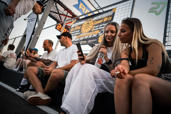 Zwei Frauen sitzen abends auf der Boxenmauer und schauen gemeinsam auf ein Handy