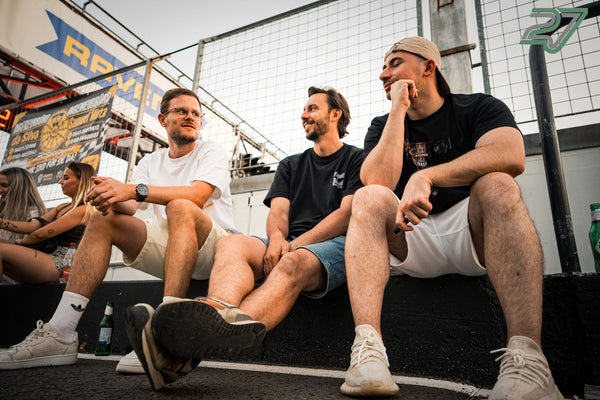 Drei Männer sitzen entspannt auf der Boxenmauer und unterhalten sich in der Abendsonne