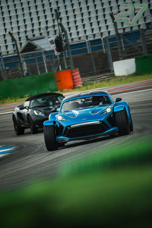 Blauer Sportwagen mit markanten Lufthutzen fährt vor einem schwarzen Roadster aus einer Kurve am Hockenheimring