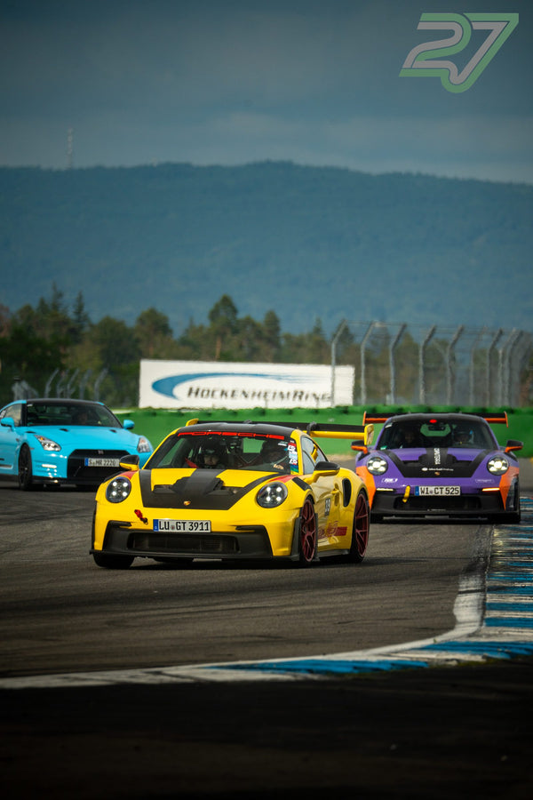 Türkiser Nissan GT-R, gelber und lila Porsche fahren dicht hintereinander am Hockenheimring