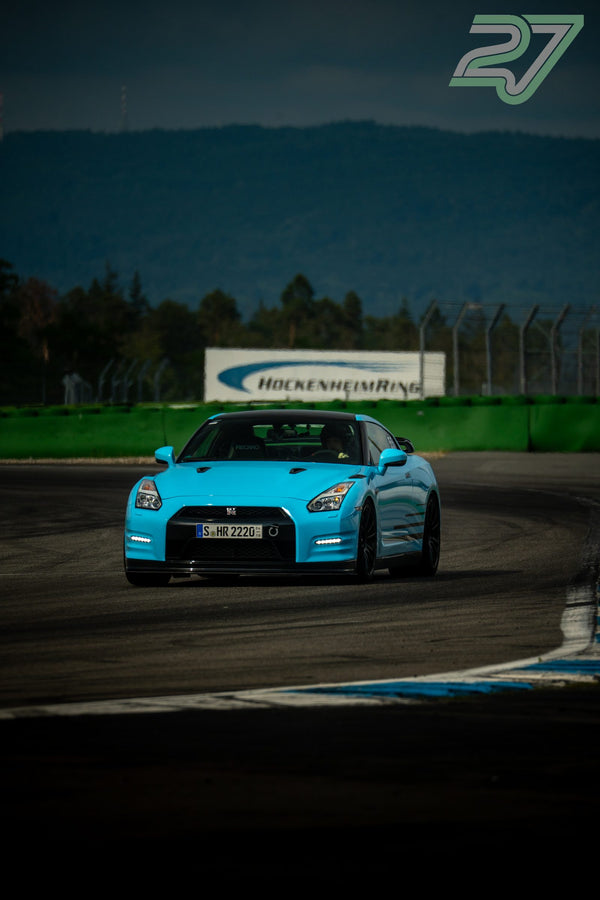 Türkisfarbener Nissan GT-R fährt bei bewölktem Himmel durch eine schnelle Kurve am Hockenheimring