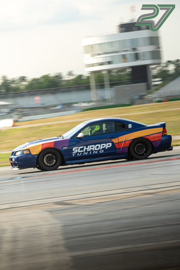 Blau lackierter Ford Mustang mit buntem Streifendesign rast mit verwischtem Hintergrund über die Strecke