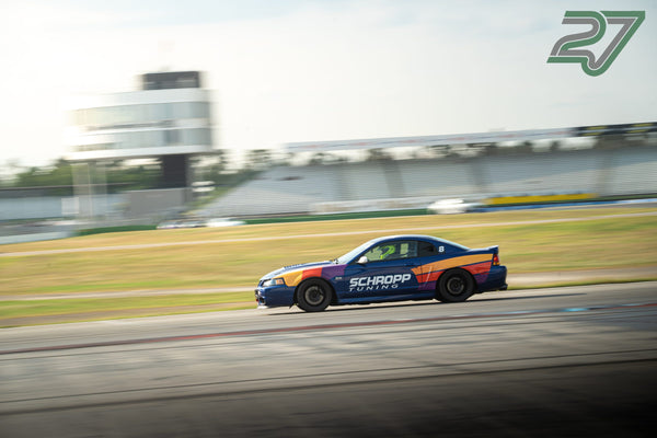 Der blaue Mustang mit bunten Streifen jagt am verschwommenen Kontrollturm vorbei