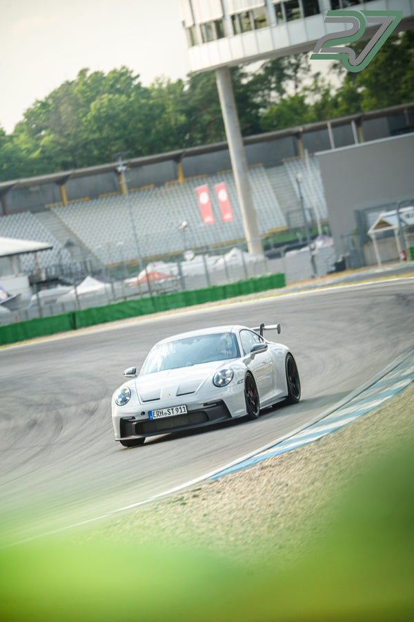 Weißer Porsche 911 GT3 mit sichtbarem Fahrer nimmt eine Kurve am Hockenheimring