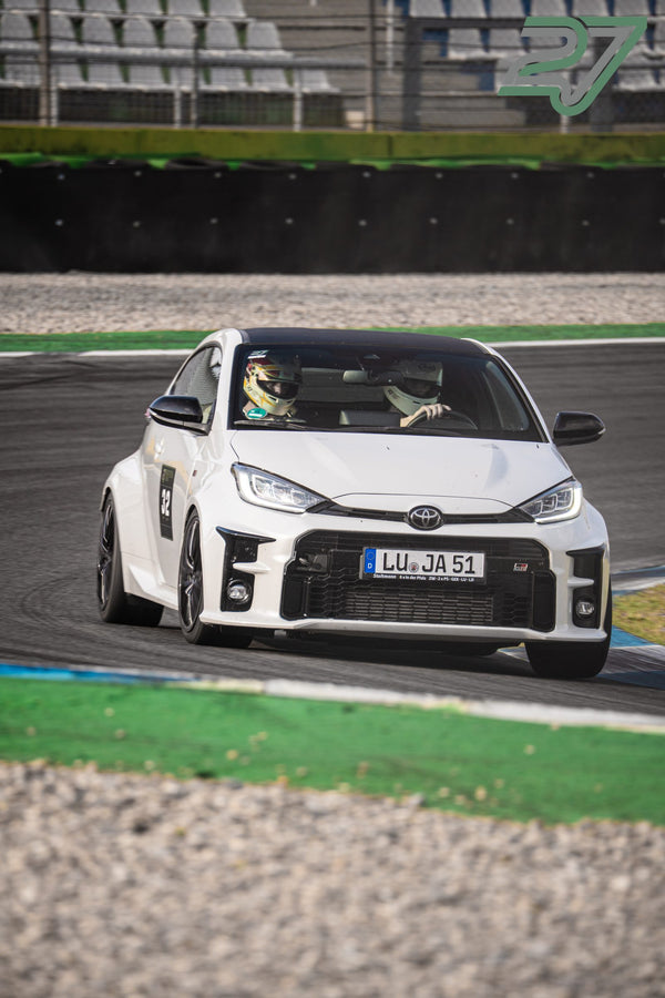 Weißer Toyota GR Yaris mit zwei behelmten Insassen fährt aus einer engen Kurve heraus