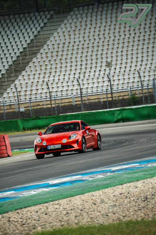 Roter Alpine A110 fährt in einer Kurve an der leeren Tribüne vorbei, roter Randstein im Vordergrund