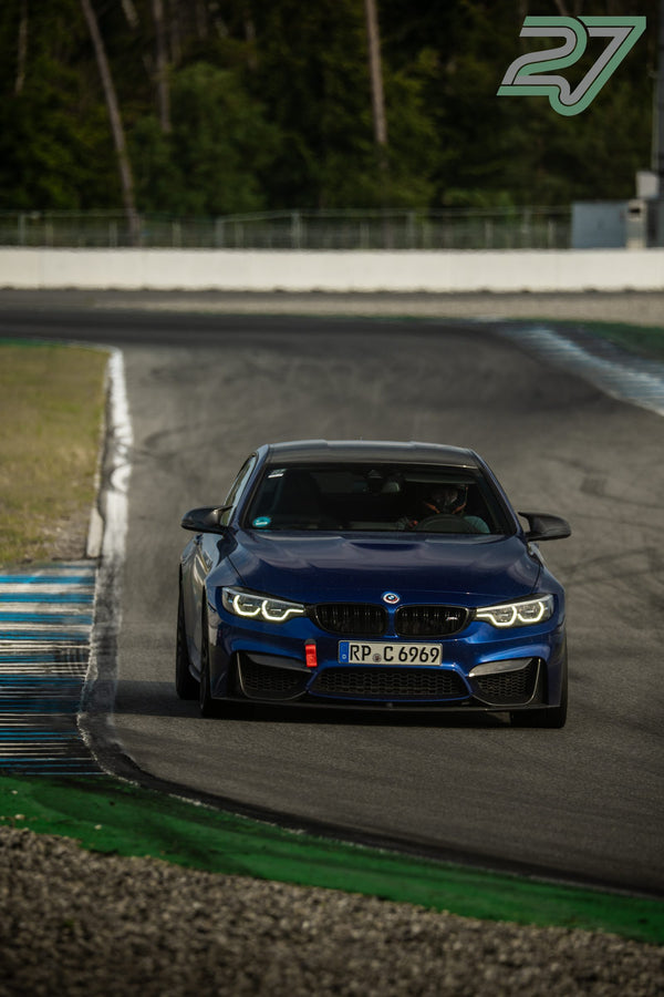 Dunkelblauer BMW M4 mit Fahrer im Helm biegt bei Tageslicht vor dichtem Wald in die Kurve