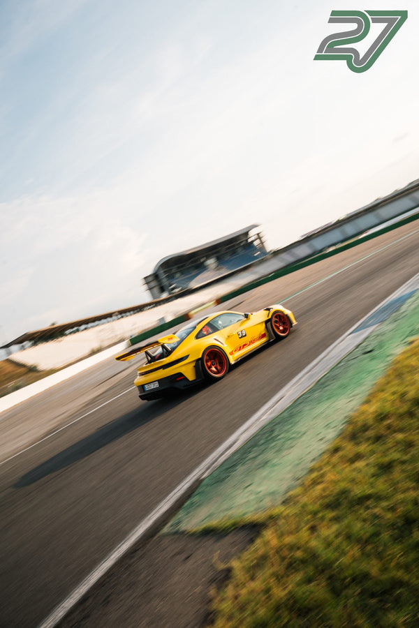 Gelber Porsche 911 GT3 RS mit roten Felgen kurvt vor der Silhouette des Kontrollturms im Abendlicht