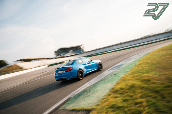Hellblauer BMW M2 fährt in einer Kurve davon, Tribüne und Hintergrund stark verwischt