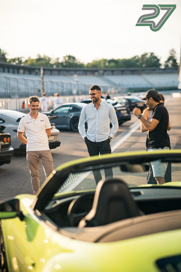 Teilnehmer unterhalten sich lachend im Abendlicht neben einem hellgrünen Cabrio im Fahrerlager