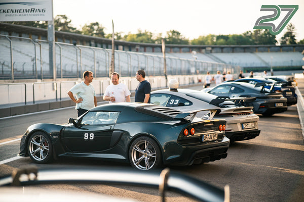 Drei Männer unterhalten sich im Abendlicht vor einem dunkelgrünen Sportwagen und weißen Porsche am Hockenheimring